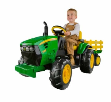 Child riding a green toy tractor with a yellow trailer with a smile.