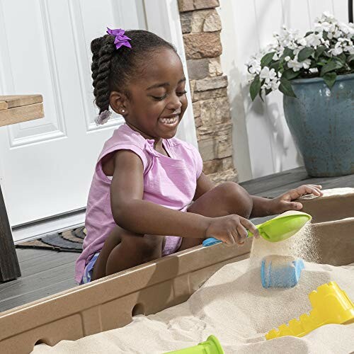 Child playing with sand in a sandbox with toys.