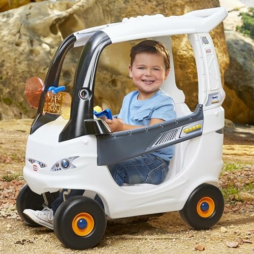 Child smiling while sitting in a white toy car outdoors.
