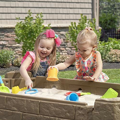 Two children playing in a sandbox with toys.