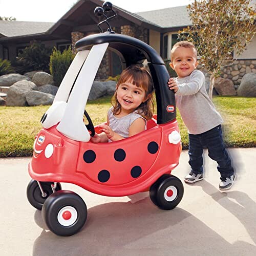 Two children playing with a red toy car outdoors.
