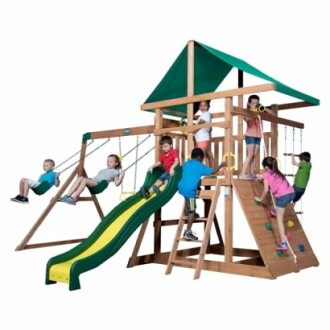 Children playing on a wooden playset with swings, slide, and climbing features.
