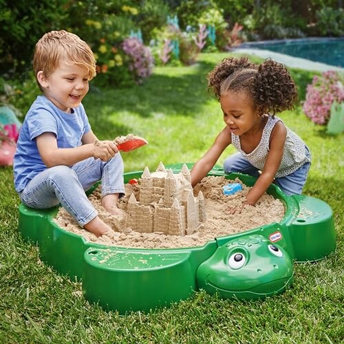 Two children playing in a turtle-shaped sandbox with sandcastles.