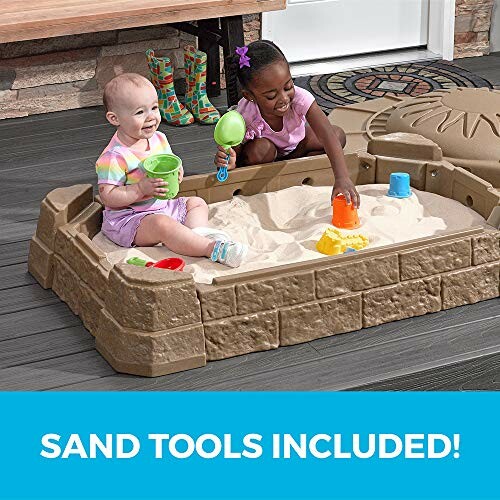 Two children playing in a sandbox with sand tools.