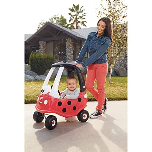 Woman pushing toddler in a red toy car shaped like a ladybug.