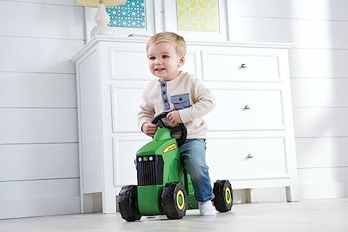 Toddler riding a green toy tractor indoors