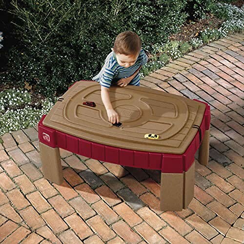 Toddler playing with toy cars on a sand and water table outdoors.