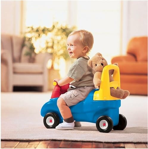 Toddler on a blue and yellow toy car with teddy bear.