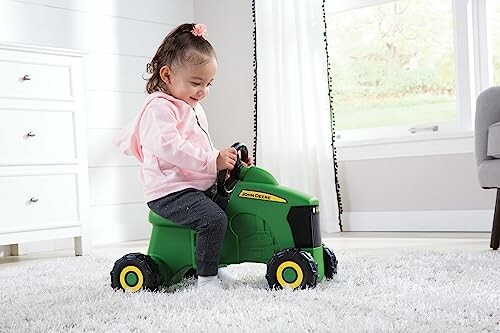 Toddler playing on green toy tractor indoors.